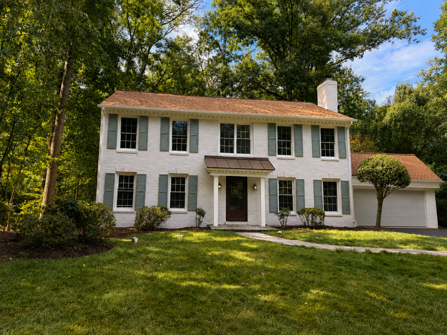 Completed white brick colonial home surrounded by mature trees
