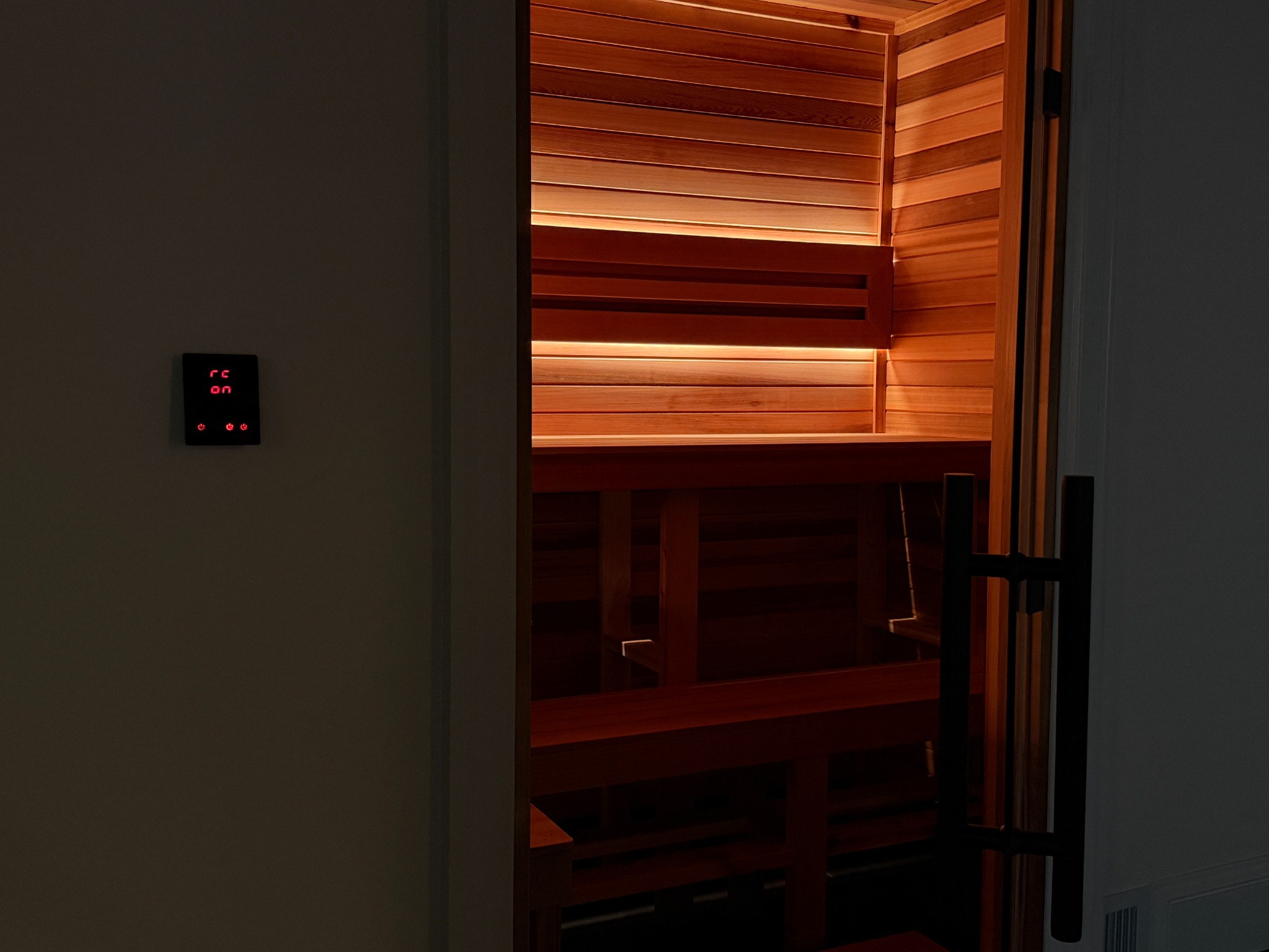 Illuminated custom cedar sauna viewed through its glass door